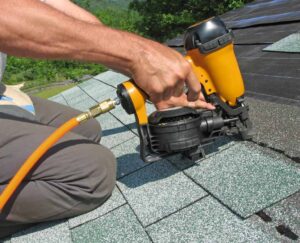 A roofer installing shingles with a nail gun