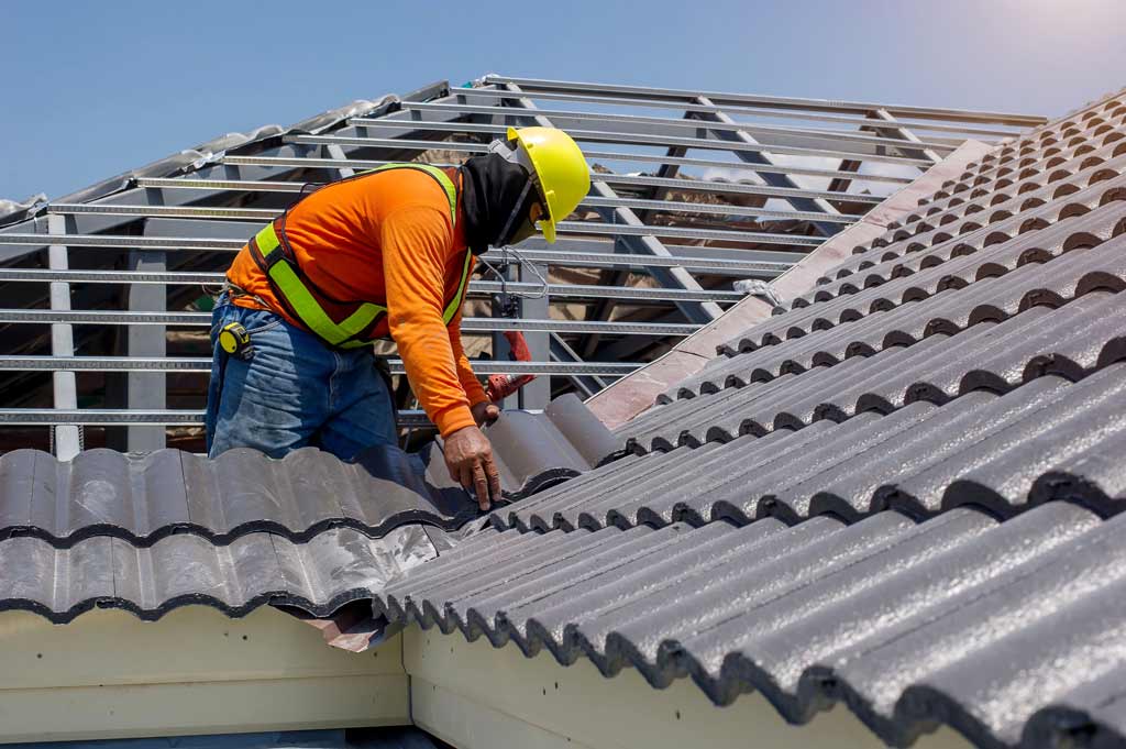 A roofer installing gray tiles on a roof 