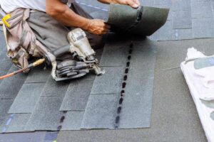 A roofer nailing down asphalt shingles