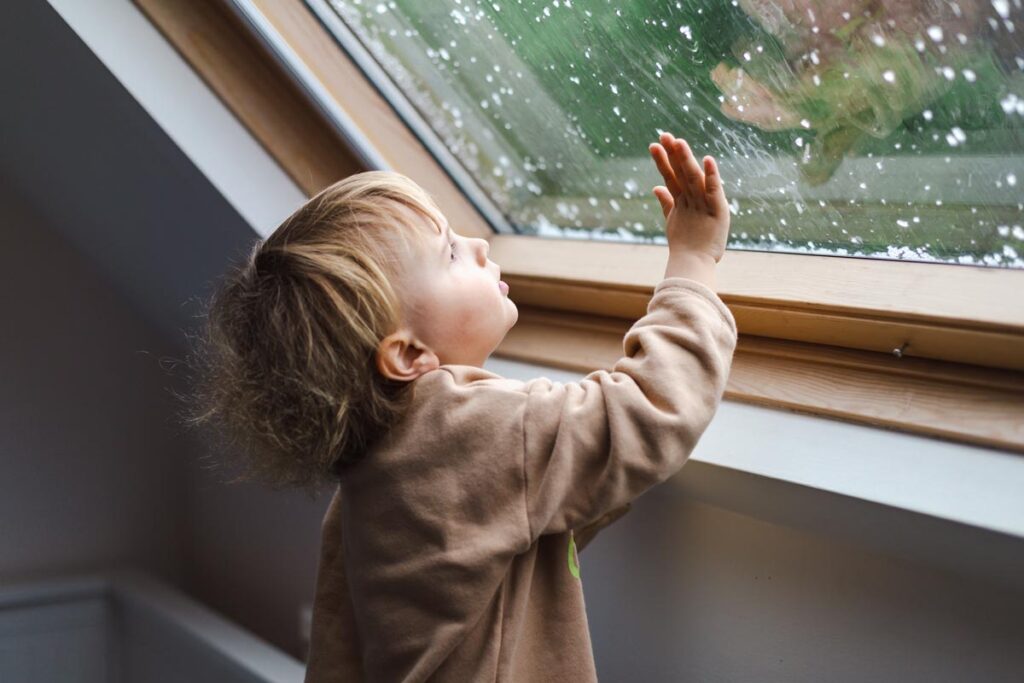 A child looking up at a window during a hail storm 